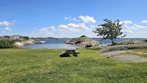 A picnic table in a grassy area with a body of water and rocky terrain in the background.