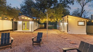 A small, single-story building with a porch, a wooden deck, and string lights. - Austin Cozy Tiny Home | Fire Pit | Pet-Friendly (Austin)