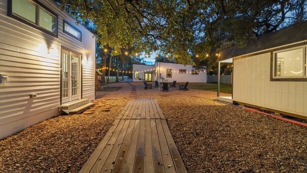 A modern RV with a wooden deck, surrounded by trees and string lights. - Austin Cozy Tiny Home | Fire Pit | Pet-Friendly (Austin)