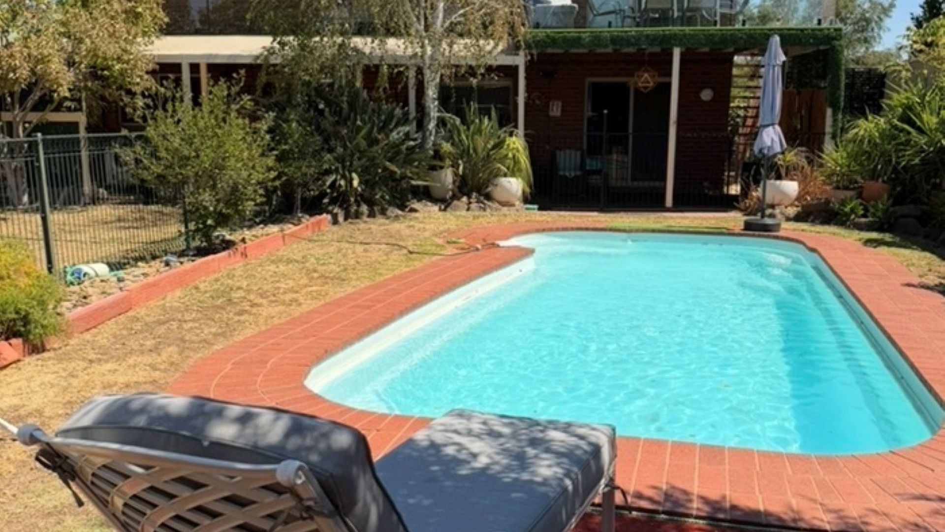 Ein rechteckiger Pool mit Backsteinbord, umgeben von Rasenflächen und verschiedenen Pflanzen.
