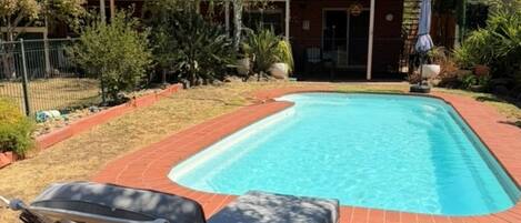 Ein rechteckiger Pool mit Backsteinbord, umgeben von Rasenflächen und verschiedenen Pflanzen.