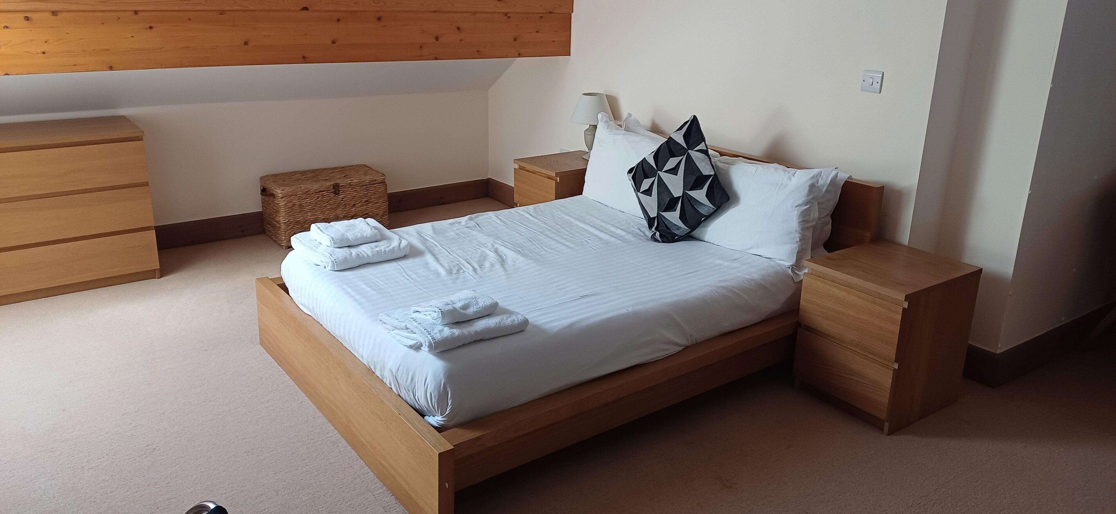 A neatly made bed with white linens and towels, wooden headboard, and bedside tables with lamps.