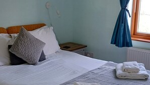 Cama bem arrumada com almofadas, mesa de cabeceira e janela com cortinas.