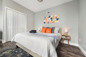A bedroom with a bed, pillows, a bedside table with a lamp, a rug, and a door. - REGAL BRICKS - Giant Outdoor Chess/Fire Pit/Game Room/Private Deck/Fire Pit (Pittsburgh)