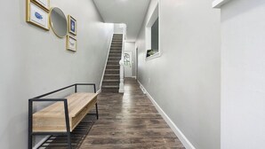 Een gang met een houten bankje, een trap en kunstwerken in lijsten aan de muur.