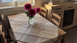 A dining area with a table set for two, a vase with flowers, and a wall clock.