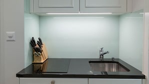 Una cocina con encimera negra, pileta de acero inoxidable y muebles blancos.