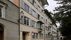 Un edificio de varios pisos con fachada color beige, contraventanas blancas y una farola.