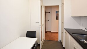 A narrow kitchen with white cabinets, a black countertop, and a tiled floor.