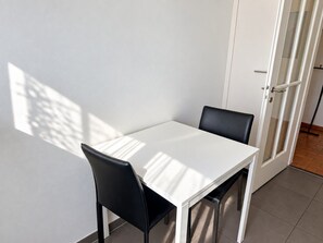 Una mesa blanca con dos sillas negras en una habitación con una puerta blanca y suelo de baldosas.