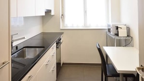 A compact kitchen with white cabinets, a black countertop, a sink, and a window above the sink.