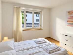 A hotel room with a bed, a bedside table, a window with curtains, and a wall-mounted artwork.