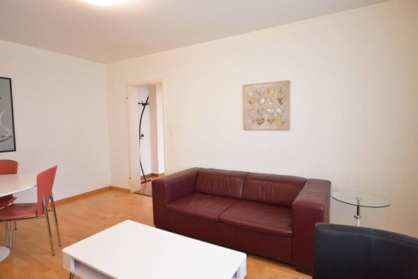 A living room with a red leather sofa, a white coffee table, and a glass table. There is a painting on the wall and a door leading to another room. - Quiet 1BR in city center - Mill 4.12 (Zürich)