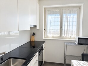 Cocina moderna con armarios blancos, encimera negra, pileta de acero inoxidable y ventana con cortinas blancas.