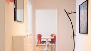 A hallway with a tiled floor, a white door at the end, and a dining area with a table and chairs.