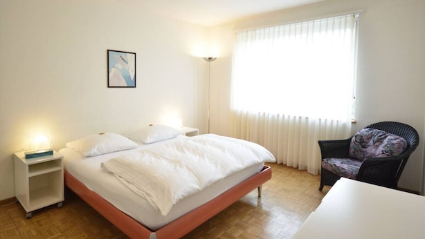 A bedroom with a bed, bedside tables, a chair, and a window with blinds.