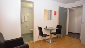A small, modern room with a wooden floor, a table with two chairs, a mirror, and a door leading to a bathroom. - Practical studio at trendy location - Stork 22 (Zürich)