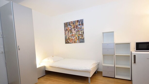 A small, modern bedroom with a single bed, a white wardrobe, a white cabinet, and a microwave. - Practical studio at trendy location - Stork 22 (Zürich)