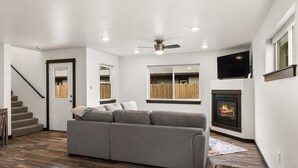 A modern living room with a gray sectional sofa, a fireplace, a TV mounted above it, and a staircase leading to another level. - Fireside Retreat (Belgrade)