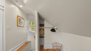 A hallway with wooden flooring, a framed picture on the wall, a window with a view of greenery, a staircase, and a basket on the floor. - Raspberry Retreat Cottage (Lovettsville)