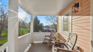 A covered porch with two rocking chairs and a small table, overlooking a green landscape and a house. - Raspberry Retreat Cottage (Lovettsville)