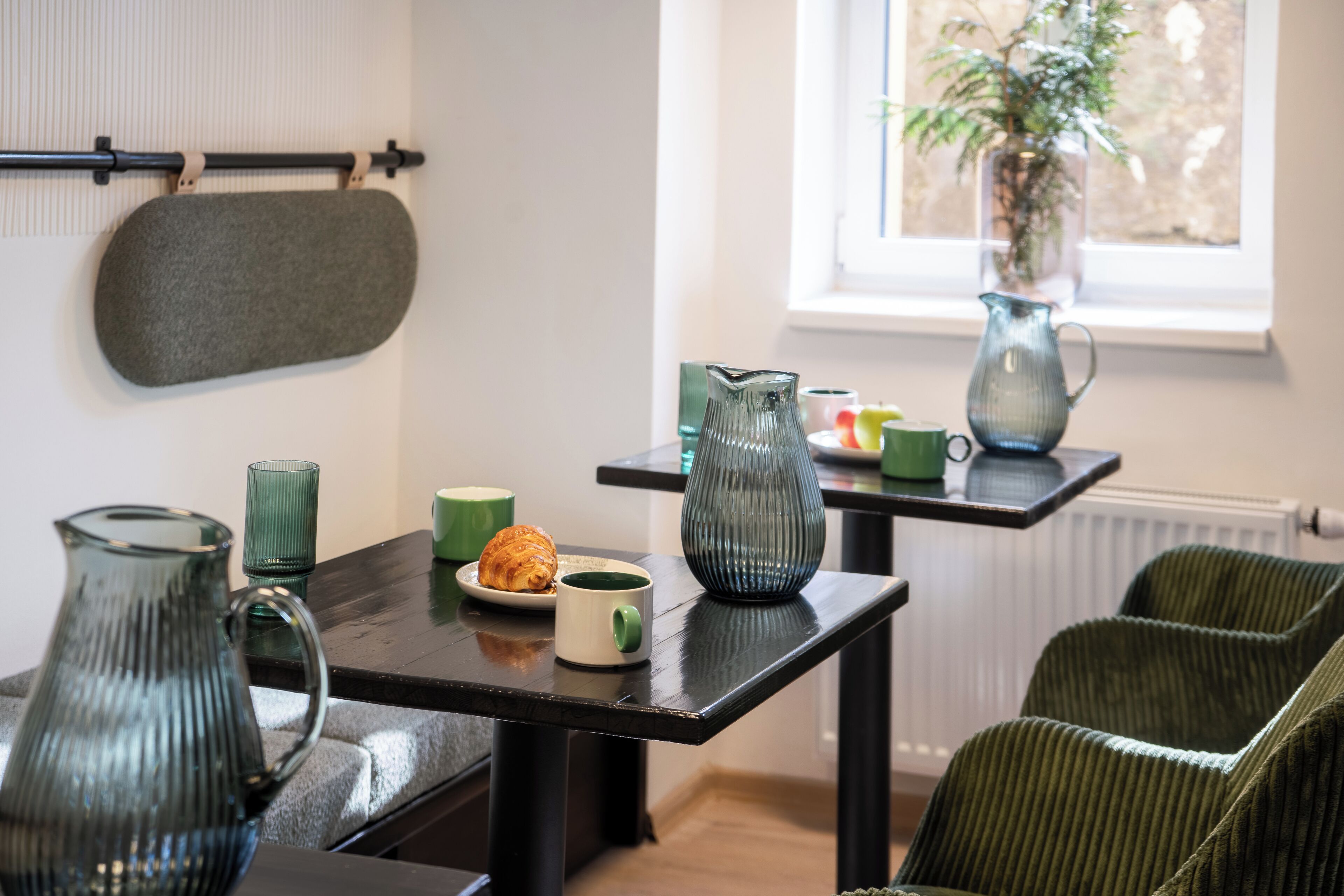 Zona pranzo con tavolo apparecchiato per due, con un croissant, una tazza verde e due caraffe.