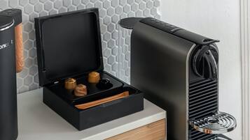 A kitchen counter with a coffee machine, a pastry, a green cup, and a tray with coffee pods.