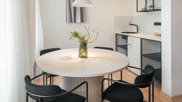 A modern dining area with a round table, black chairs, a white pendant light, and a vase with greenery.