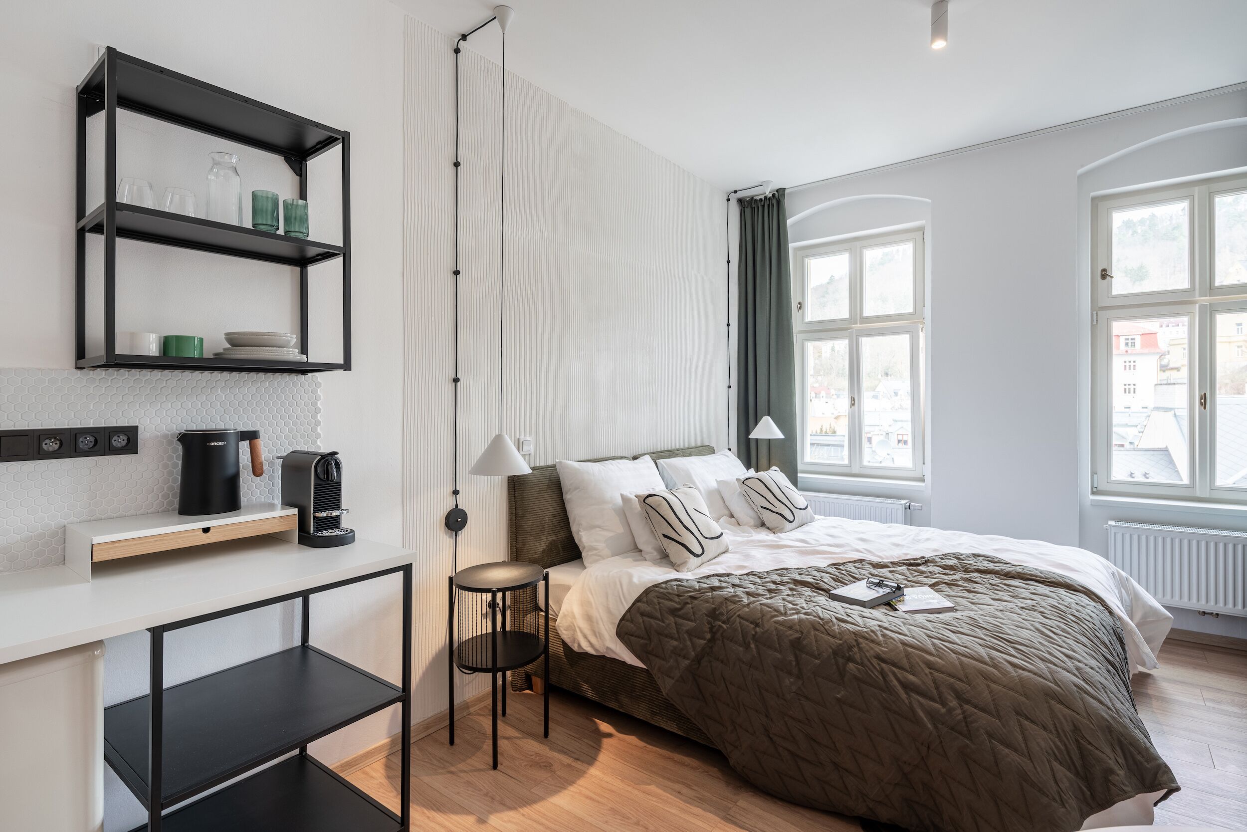 Une chambre moderne avec un lit, des tables de chevet, une étagère contenant des ustensiles de cuisine et de grandes fenêtres.