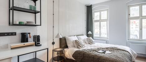 A modern bedroom with a bed, bedside tables, a shelf with kitchen items, and large windows.