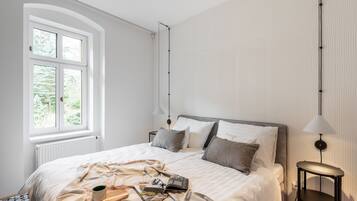 Ett sovrum med en säng, ett sängbord, en lampa, ett fönster och ett element.