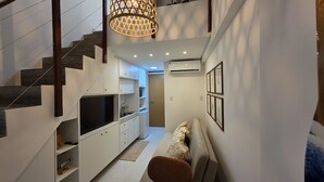 A modern interior with a staircase, built-in TV, white cabinetry, and a decorative wall piece. - Duplex Vista Piscina 313c Bela Vista bLP (Ipojuca)