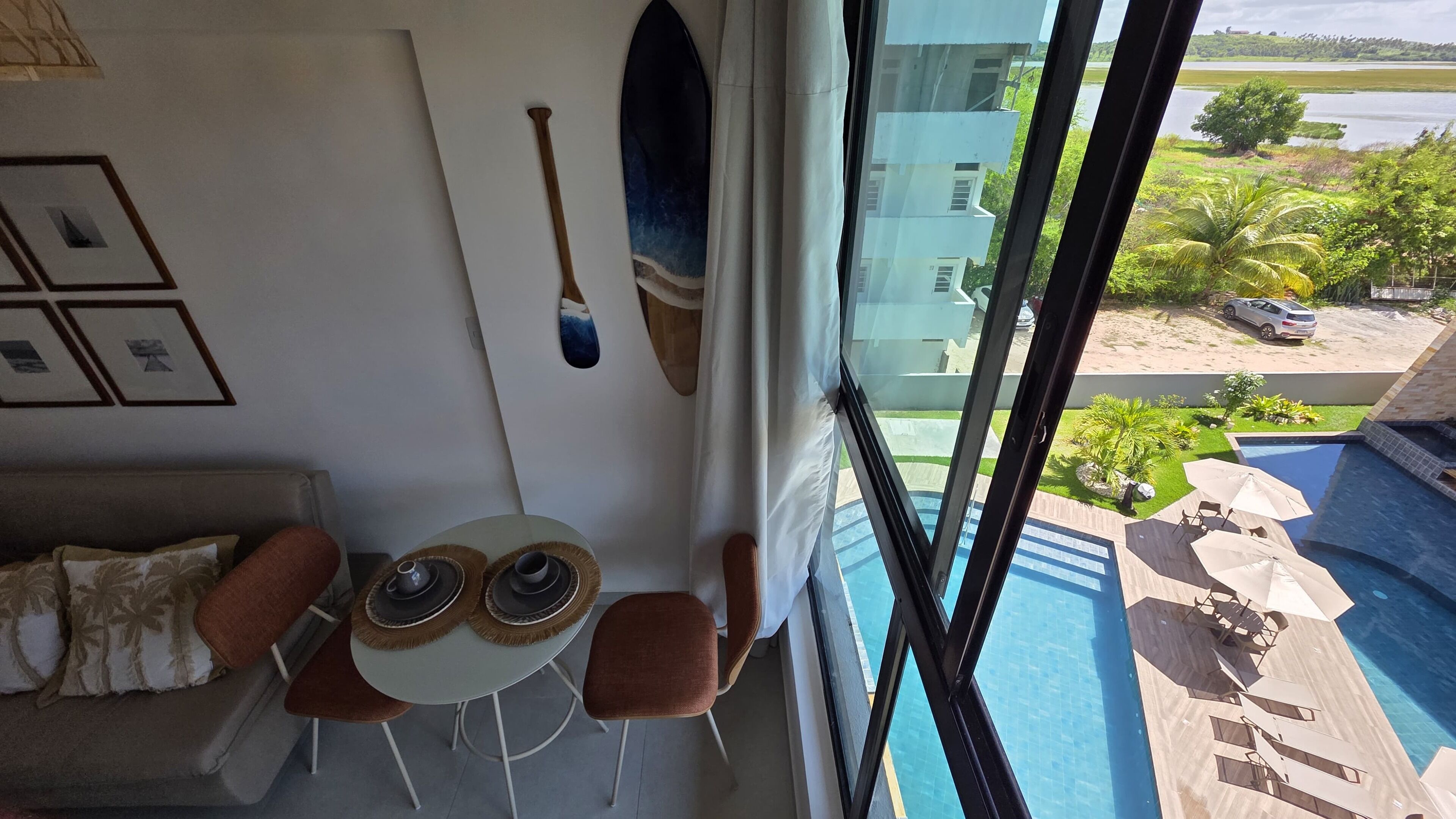 Un balcón con vista a una piscina, una mesa con sillas y un sofá con cojines.