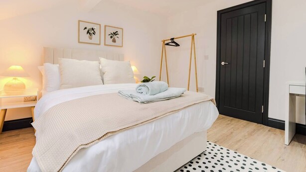 A neatly made bed with a white comforter and a rolled towel, a bedside lamp, and two framed pictures on the wall. - Stunning Sky view 2 BR Flat - Free WIFI, Parking (Harehills)