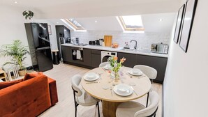 A modern kitchen with a dining area, featuring a round table set for four, a sofa, and a skylight above the kitchen. - Stunning Sky view 2 BR Flat - Free WIFI, Parking (Harehills)