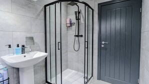A modern bathroom with a glass-enclosed shower, a white sink with a mirror, and a dark wooden door. - Stunning Sky view 2 BR Flat - Free WIFI, Parking (Harehills)