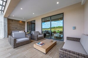 Uma área externa moderna para relaxar, com móveis de vime, uma mesa de centro de madeira e uma porta de vidro que dá para um pátio.
