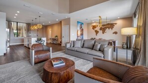 A spacious living area with a sofa, leather chairs, and a coffee table. There is a world map on the wall, a lamp, and a view of the kitchen in the background. - Disney Vacation Rental | 3BR Luxury Townhouse (Kissimmee)