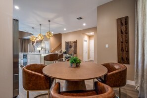 A dining area with a round table, four brown chairs, and pendant lights.