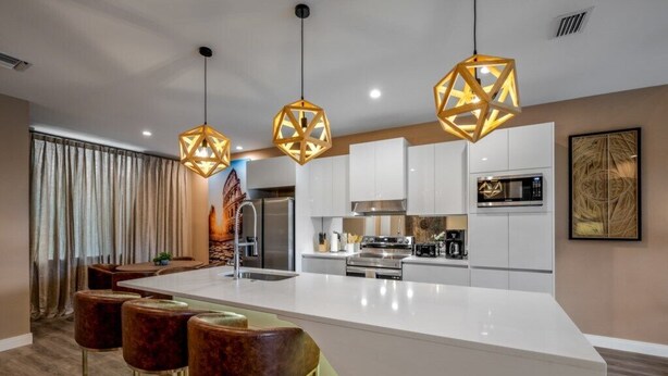 Une cuisine moderne dotée d’un grand îlot central, de luminaires suspendus et de tabourets de bar.