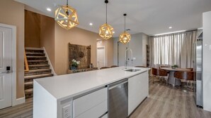 Une cuisine moderne dotée d’un îlot central, de luminaires suspendus et d’un coin repas avec une table et des chaises.