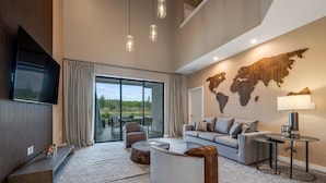 A modern living room with a large flat-screen TV, a world map wall, a sofa, a coffee table, and a lamp. - Stylish Townhouse Near Disney for Families (Kissimmee)