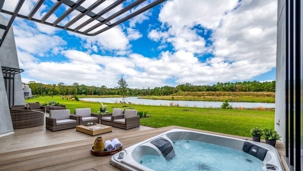 A hot tub on a wooden deck with wicker furniture and a view of a lake and greenery. - Stylish Townhouse Near Disney for Families (Kissimmee)