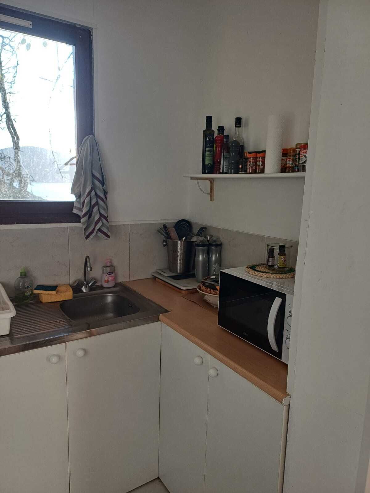 A small kitchen with a sink, countertop, and a microwave. There are shelves above the counter holding various kitchen items.