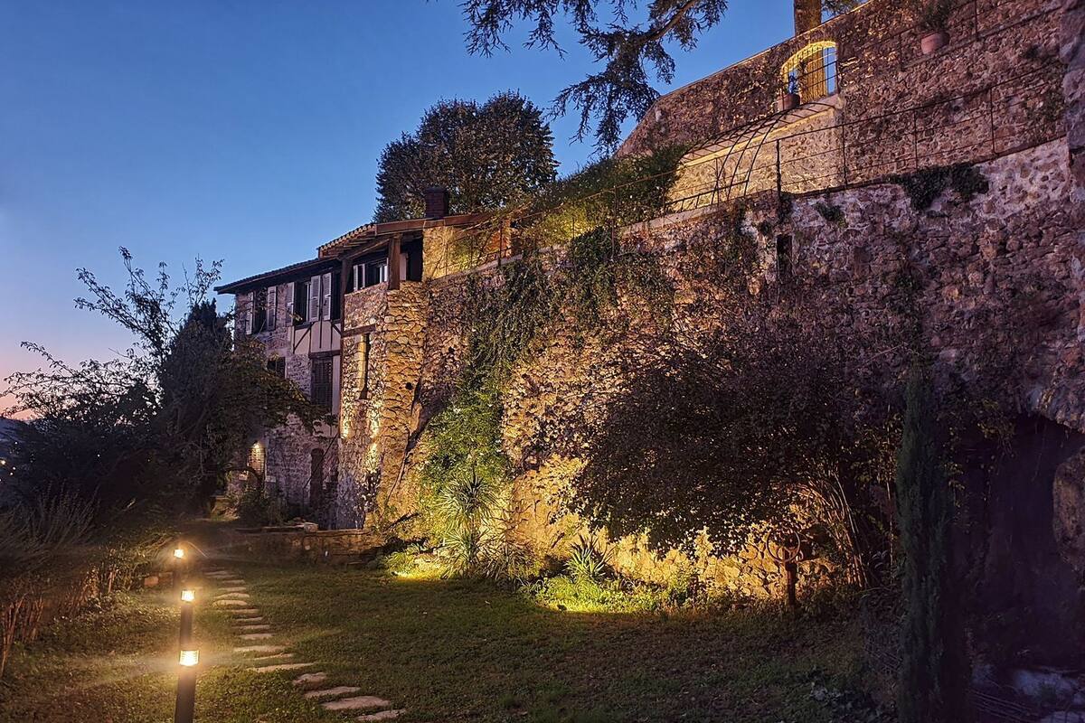 A stone building with a rustic exterior, a stone pathway leading to the entrance, and a well-lit garden area.