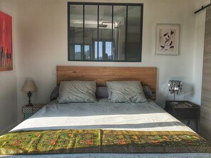 A bedroom with a wooden headboard, two pillows, a patterned bedspread, a nightstand with a lamp, and a framed picture on the wall. - La Bâtie (Vienne)