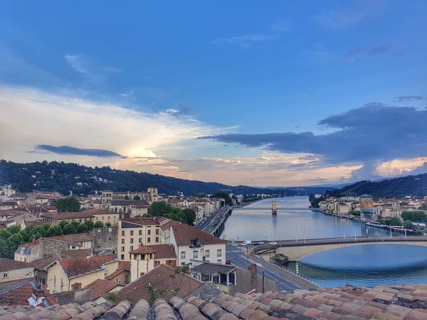 A river with a bridge, buildings, and hills in the background.