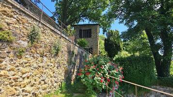 A stone wall with a small stone building, a wooden pathway, and lush greenery.