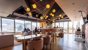 A modern interior with a bar area, seating arrangements, and large windows offering city views.