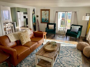 A living room with a brown leather sofa, a wooden coffee table, a green armchair, and a painting on the wall.